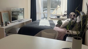 Ein modernes Hotelzimmer mit Bett, Nachttisch, Fernseher und einem großen Fenster mit Vorhängen.