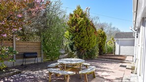 Un patio con una mesa redonda de madera y bancos, rodeado por una cerca de madera y varios árboles.