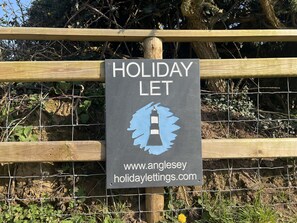 A sign for 'Holiday Let' with a lighthouse graphic and a website URL.