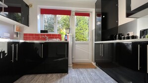 Una cocina moderna con gabinetes negros, un visillo rojo en la ventana y vistas al exterior con vegetación.