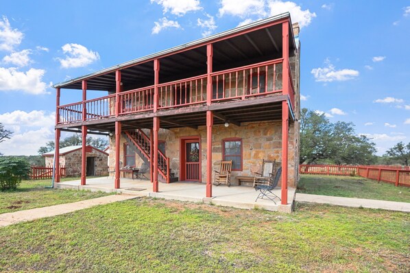 A two-story stone building with a red balcony and a staircase leading to the upper level. - Stein Haus Ranch 4 Bedroom Home by RedAwning (Castell)