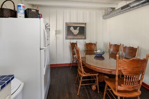 A compact kitchen with a refrigerator, a dining table with wooden chairs, and a wall-mounted picture of a rooster. - Stein Haus Ranch 4 Bedroom Home by RedAwning (Castell)