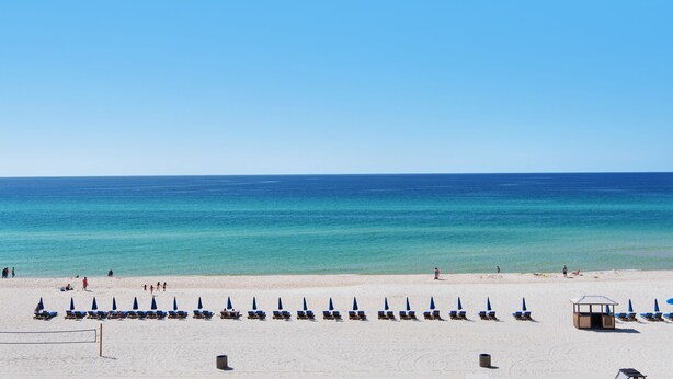 A beach with rows of sun loungers and umbrellas, a lifeguard tower, and the ocean in the background. - ☀️Great Views, Close to Beach-Laketown Wharf 838☀️ (Panama City Beach)