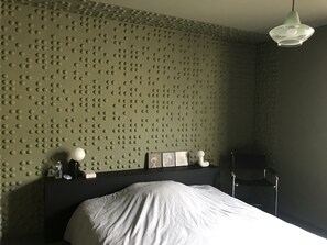 Cozy retreat with a textured wall and a comfortable bed, featuring a bedside table and lamp.