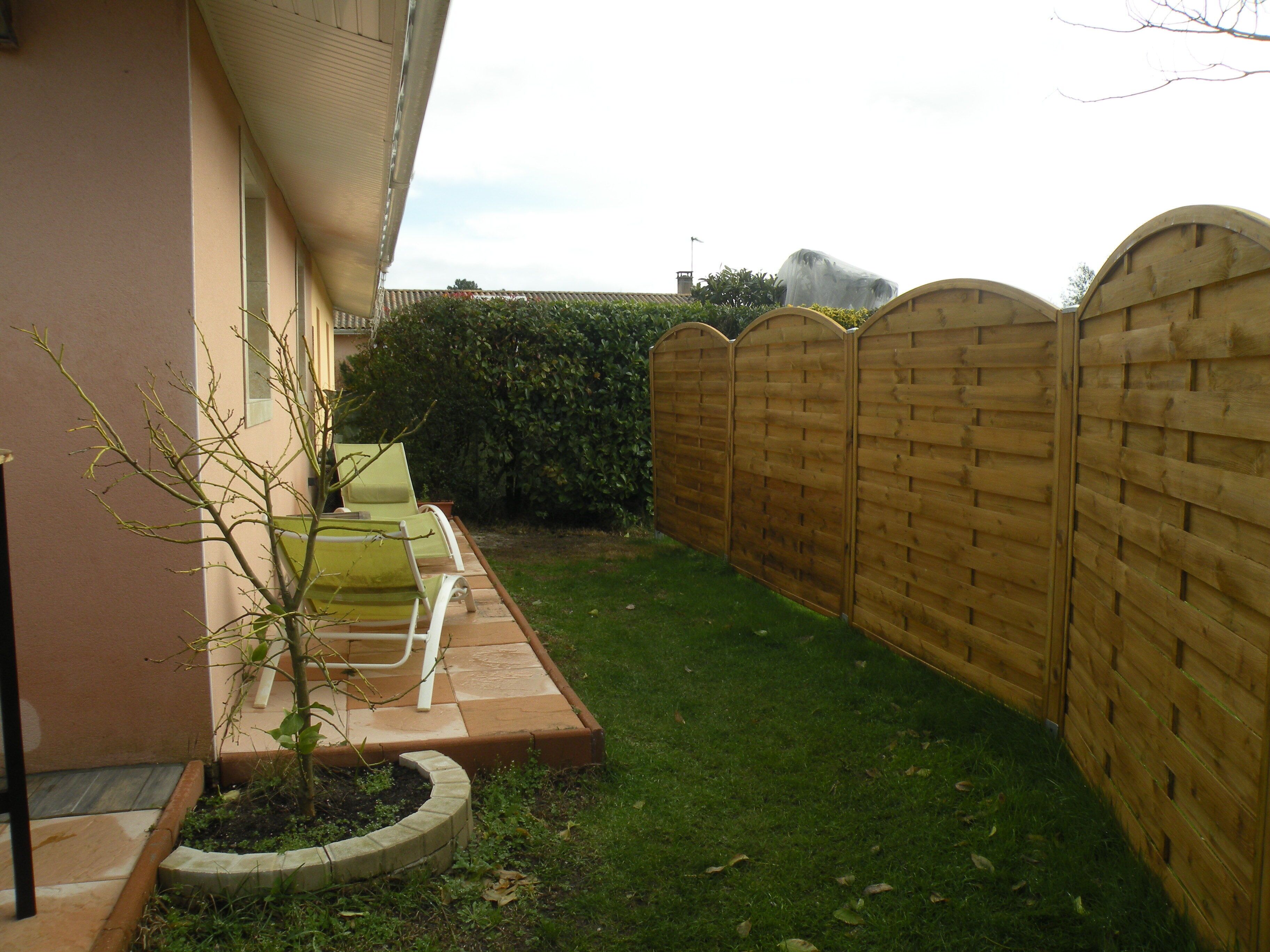 Un petit jardin clos, avec une clôture en bois, un petit arbre et un espace aménagé avec un banc et une table.