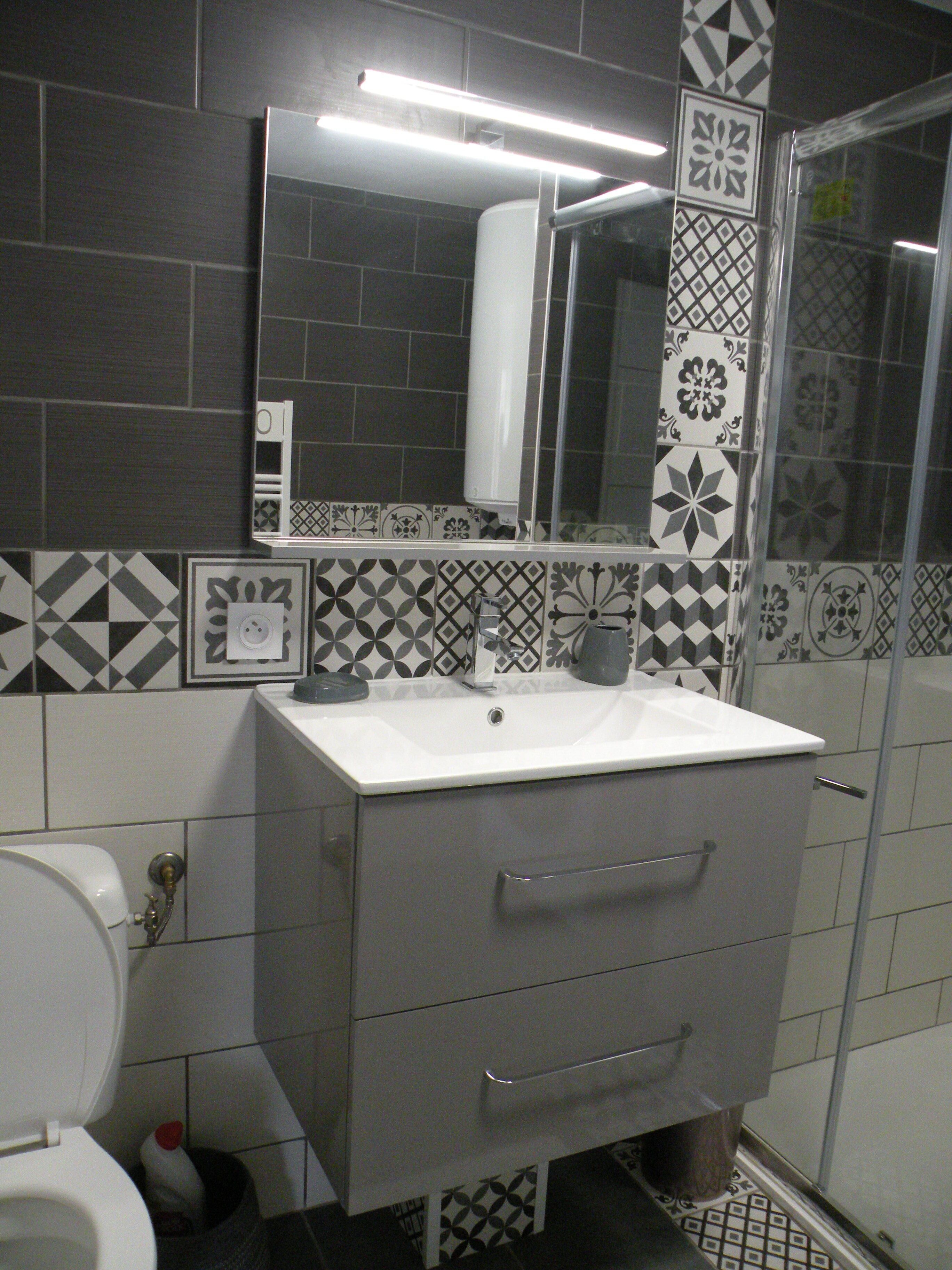 Une salle de bain avec un lavabo blanc, un miroir au-dessus et des carreaux décoratifs sur les murs.