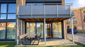 A modern outdoor seating area with a glass enclosure, a wooden bench, and a table.