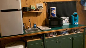 Cocina compacta con refrigerador, microondas y cafetera sobre una encimera de madera.