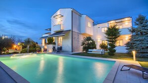 A modern two-story house with a swimming pool, outdoor seating, and a well-lit garden at dusk. - Villa Aylin, 5-bed, Next to the sea (Medulin)