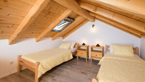Une petite chambre mansardée, chaleureuse et accueillante, avec deux lits simples, des meubles en bois et un puits de lumière.