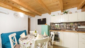 Un coin repas avec une table dressée pour deux personnes, une cuisine avec des meubles blancs et un dosseret carrelé, et un plafond en bois.