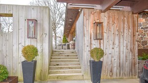 A wooden staircase leading to a house with a stone wall, two potted plants, and a car parked outside. - The Clubhouse - On Golf Course - Serene Retreat (Searcy)
