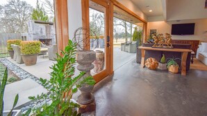 A spacious living area with a large sliding glass door leading to an outdoor patio, a wooden coffee table, and various potted plants. - The Clubhouse - On Golf Course - Serene Retreat (Searcy)