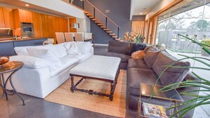 A modern living room with a sofa, ottoman, and coffee table, a staircase, and a view of the outdoors. - The Clubhouse - On Golf Course - Serene Retreat (Searcy)