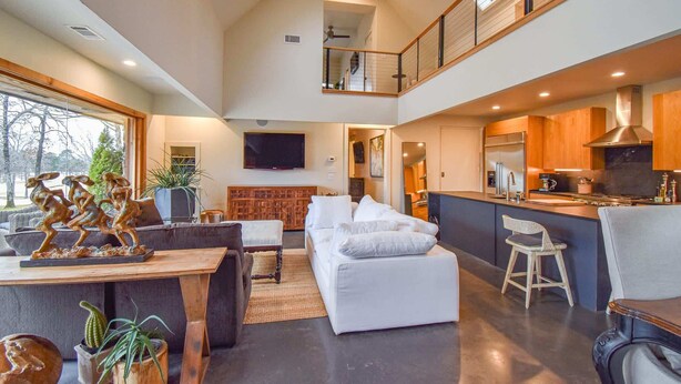A spacious living area with a high ceiling, a kitchen with modern appliances, and a balcony with a railing. - The Clubhouse - On Golf Course - Serene Retreat (Searcy)