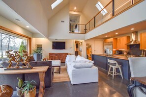 A spacious living area with a high ceiling, a kitchen with modern appliances, and a balcony with a railing. - The Clubhouse - On Golf Course - Serene Retreat (Searcy)