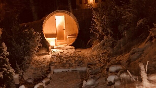 A snow-covered pathway leading to a circular wooden structure with a door, surrounded by snow-laden trees and a small pond. - Das Alte Forsthaus Spiegelhütte Wohnung Wildbach (Lindberg)