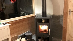 A cozy room with a wood-burning stove, a window with decorations, and a wooden floor. - Das Alte Forsthaus Spiegelhütte Wohnung Wildbach (Lindberg)