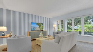 A modern living room with a TV, sofa, and coffee table, featuring striped wallpaper and large windows.