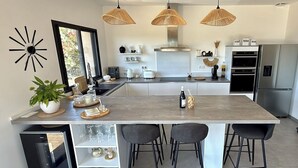 Een moderne keuken met een centraal eiland, barstoelen, hanglampen en een ingebouwde wijnkoeler.