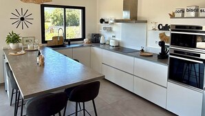 Een moderne keuken met een groot eiland, hangende lampen en uitzicht op groen.