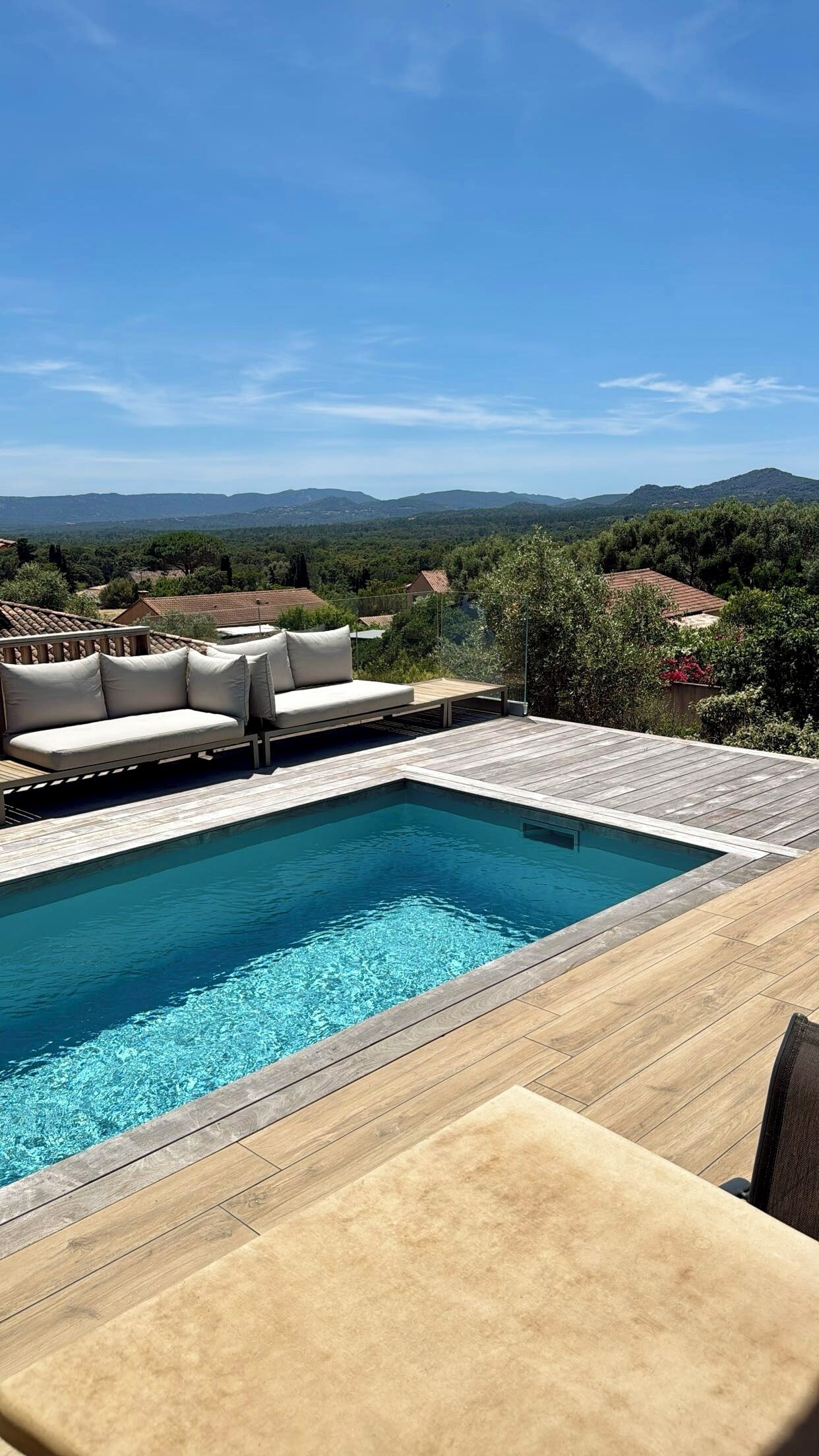 Una piscina con cubierta de madera, un sofá y vistas del paisaje circundante.