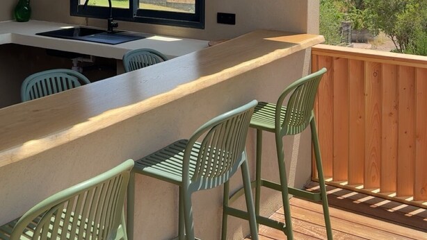 Een houten terras met een bar, twee hangende lampen, een raam met uitzicht op bomen en een houten balustrade.