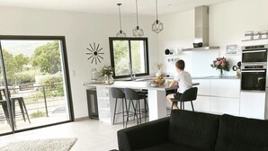 Een moderne keuken met een groot eiland, zwarte barstoelen en hanglampen.