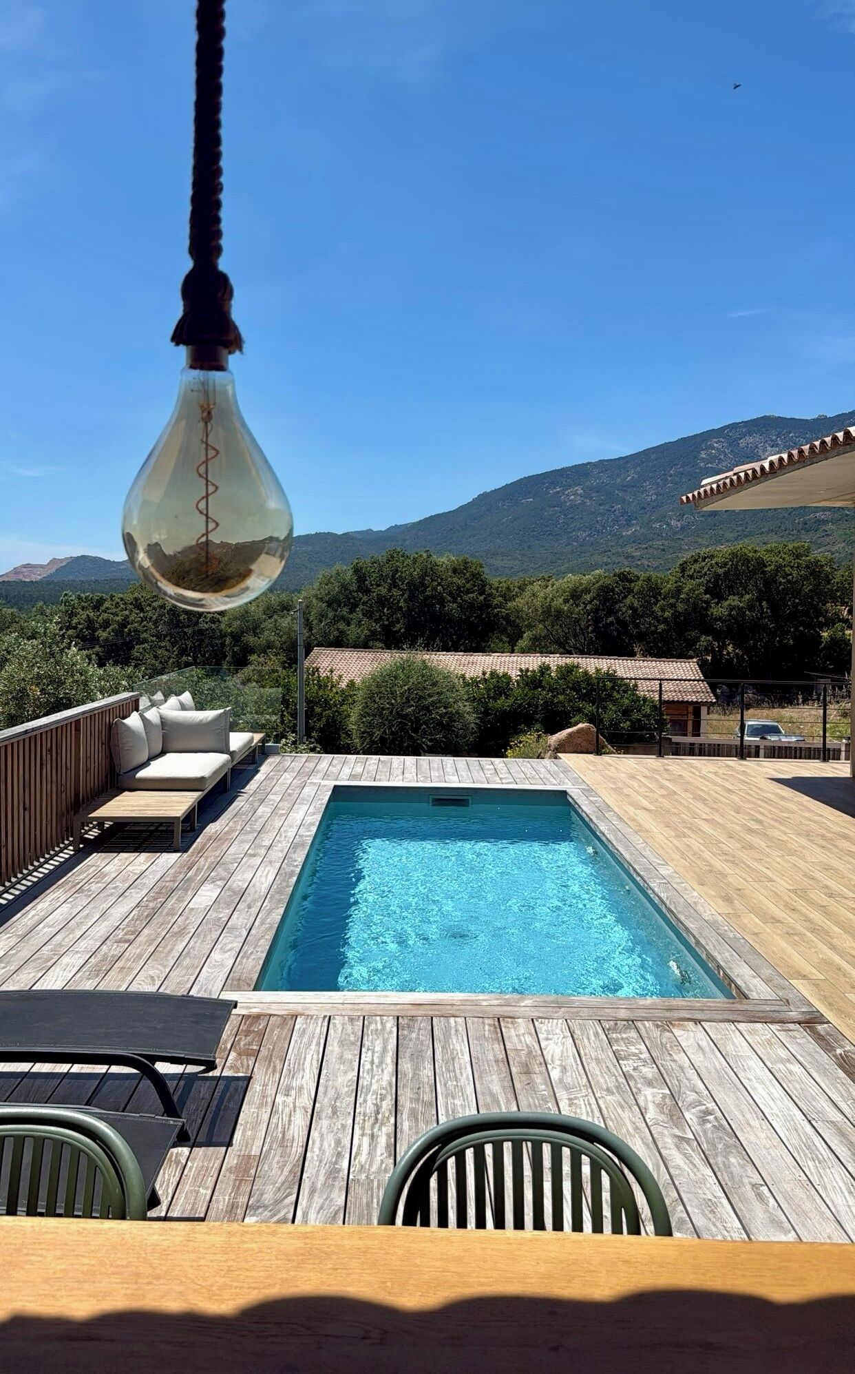 Una terraza de madera con piscina, una lámpara colgante y vistas a las montañas.