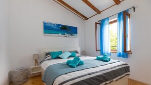 A bedroom with a bed, a painting of a beach scene, a window with blue curtains, and a wooden floor. - Amazing home in Porec (Porec)