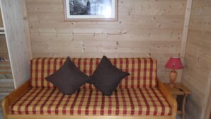 En soffa i trä med en rutig kudde, två mörka kuddar och ett litet bord med en röd lampa.