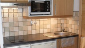 Ett kompakt kök med träskåp, en inbyggd mikrovågsugn, en diskmaskin och en kakelbeklädd vägg bakom arbetsbänken.