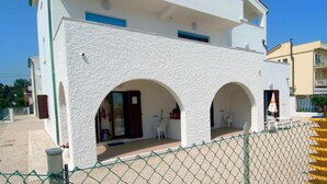 Ein Gebäude mit weißer Fassade, zwei Rundbögen und einem eingezäunten Bereich mit Außenbestuhlung.