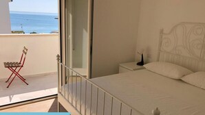 Ein Schlafzimmer mit Bett, Nachttisch, Sessel und Meerblick.