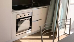Eine kompakte Küche mit Herd, Backofen und Spüle, eine Schiebetür zu einem Balkon und einem Stuhl.