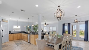 A spacious kitchen with wooden cabinets, a dining area with a large table and chairs, and a view through the glass doors.