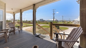 A covered porch with wooden chairs and a view of a road and buildings.