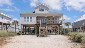 A beachfront house with a covered porch and a staircase leading to the main floor.