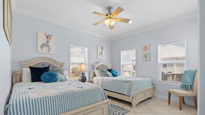 A bedroom with two beds, a ceiling fan, and artwork on the walls.