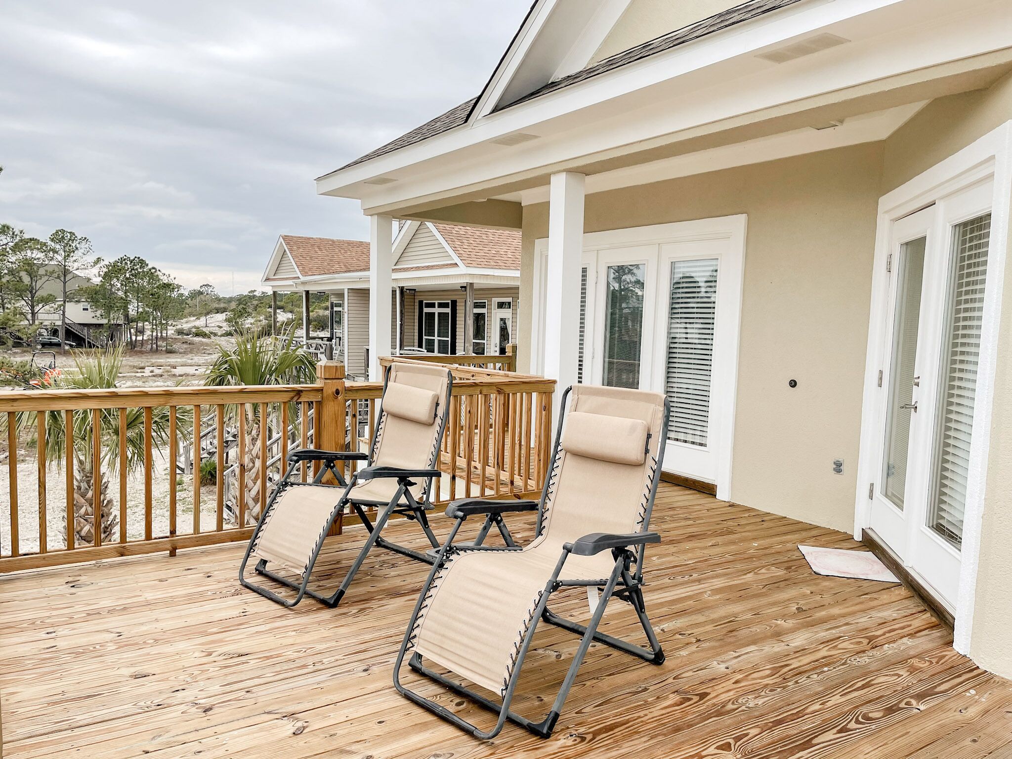 A covered deck with four lounge chairs and a wooden railing.