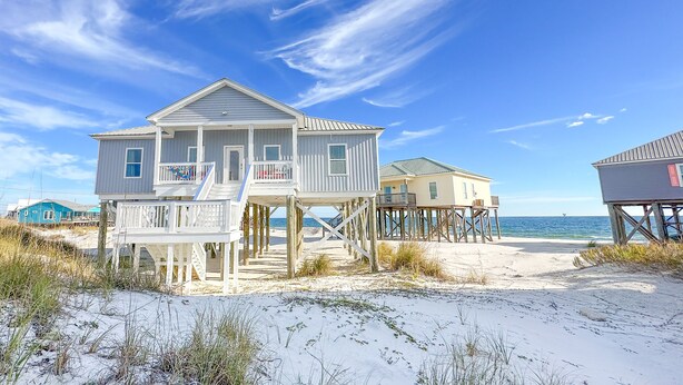 A beachfront house with a two-story structure, a balcony, and a wooden deck. - Dauphin Tale - Family Friendly Gulf View Home only Steps to Gulf of Mexico (Dauphin Island)