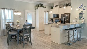 A modern kitchen with white cabinets, stainless steel appliances, and a central island with bar stools. - Dauphin Tale - Family Friendly Gulf View Home only Steps to Gulf of Mexico (Dauphin Island)