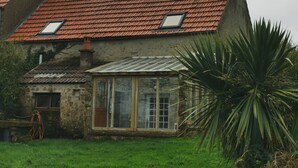 Una casa in pietra rustica con tetto in tegole rosse e una piccola serra in vetro.