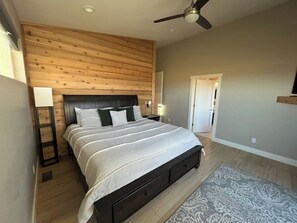 Un dormitorio con cama, cabecera de madera, mesitas de noche, una lámpara de pie y un ventilador de techo.