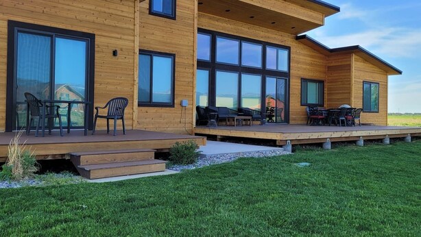 Une maison moderne en bois, dotée de grandes fenêtres et d’un patio couvert.