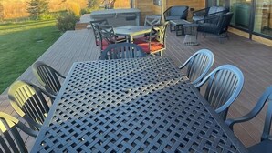 A deck with a table and chairs, overlooking a grassy field and mountains. - Indoor/Outdoor Living with 4-Peak Teton View (Driggs)