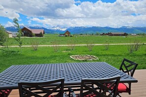 Un espacio de estar al aire libre con una mesa y sillas, un campo cubierto de césped y una cadena montañosa al fondo.