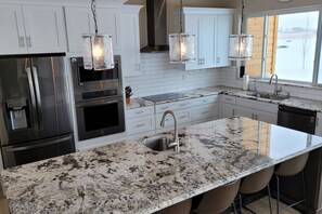 A modern kitchen with stainless steel appliances, a granite countertop, and pendant lighting.