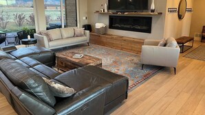 A modern living room with a sectional sofa, a white armchair, a fireplace, and a large TV. - Indoor/Outdoor Living with 4-Peak Teton View (Driggs)