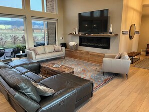 A modern living room with a sectional sofa, a white armchair, a fireplace, and a large TV.